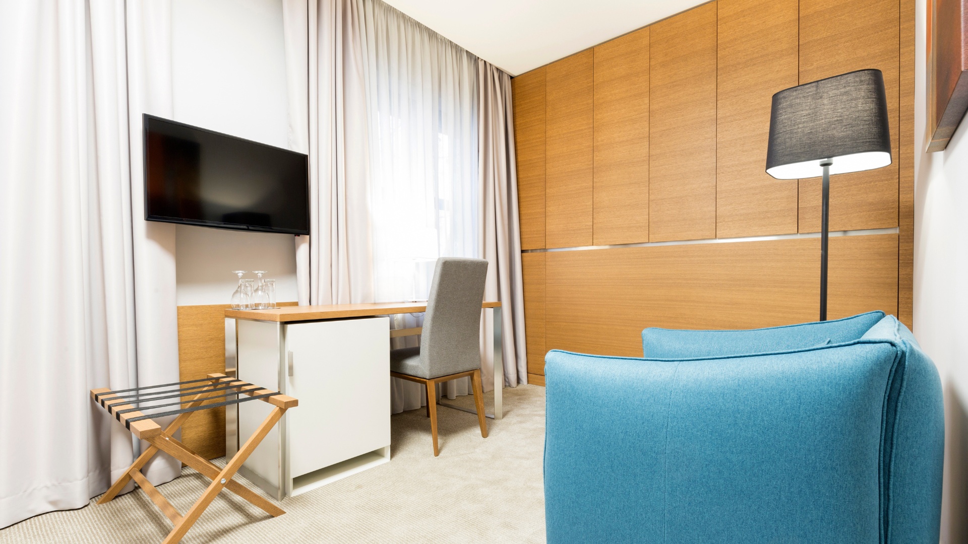 Hotel guest room accessories Whitmor foldable hotel luggage rack with durable straps, designed for guest convenience and organization. Shown in a modern hotel room featuring a USB charging clock, minibar fridge, and curated in-room amenities for an elevated stay.